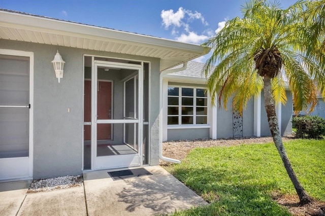 view of exterior entry featuring a yard and stucco siding