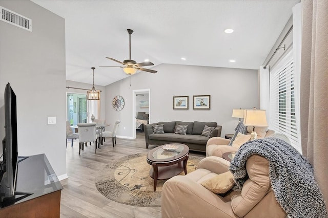 living area featuring a ceiling fan, visible vents, vaulted ceiling, baseboards, and light wood-type flooring