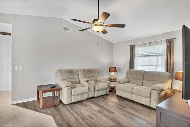 living area featuring visible vents, ceiling fan, vaulted ceiling, a textured ceiling, and light wood-type flooring