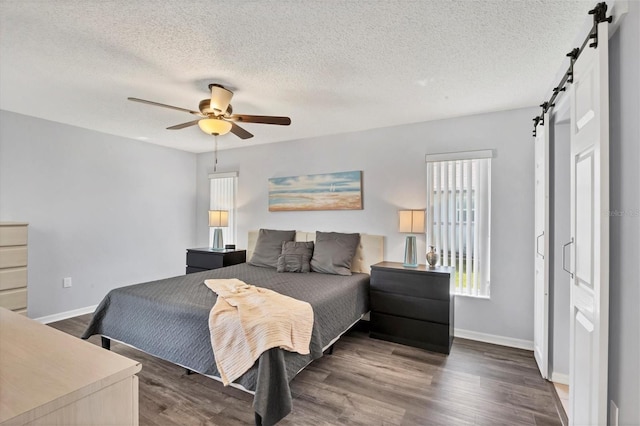 bedroom with ceiling fan, a barn door, wood-type flooring, and a textured ceiling