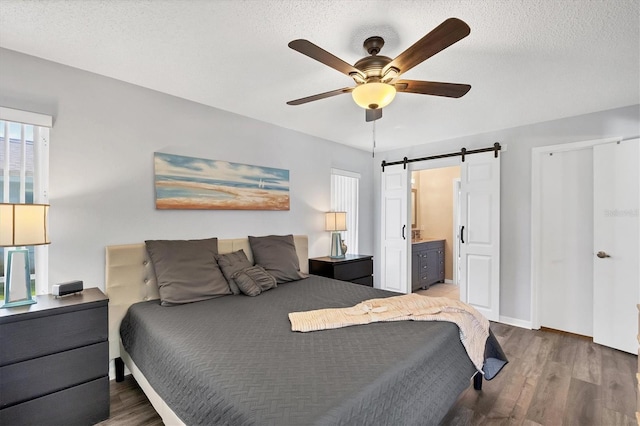 bedroom with dark wood-style floors, a barn door, ceiling fan, a textured ceiling, and ensuite bath