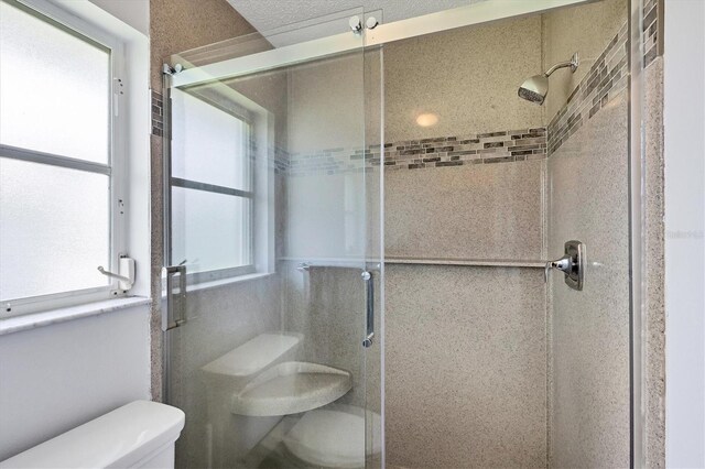 bathroom featuring a shower with door and toilet