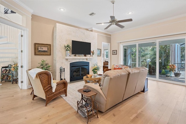 living room with ceiling fan, ornamental molding, light wood-type flooring, and a large fireplace