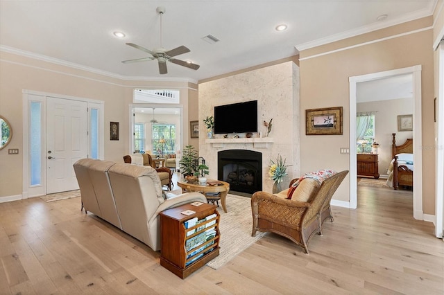 living room featuring light wood-type flooring, ornamental molding, a large fireplace, and ceiling fan