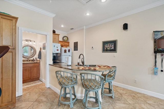 kitchen with kitchen peninsula, white refrigerator, ornamental molding, stone counters, and a kitchen bar