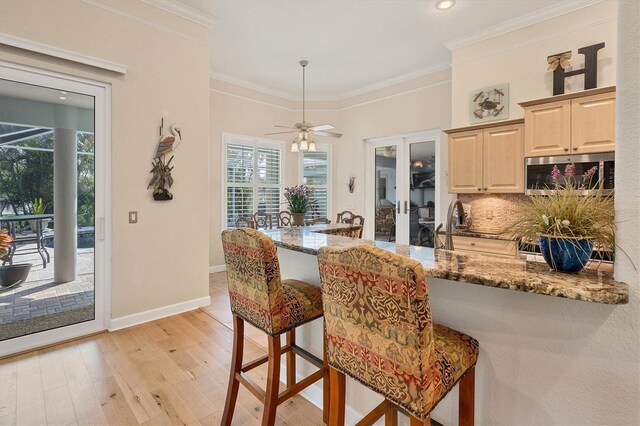 kitchen with light wood-type flooring, a breakfast bar, stone counters, crown molding, and decorative backsplash