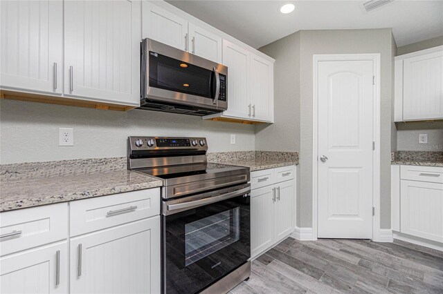 kitchen featuring light hardwood / wood-style flooring, appliances with stainless steel finishes, light stone countertops, and white cabinetry