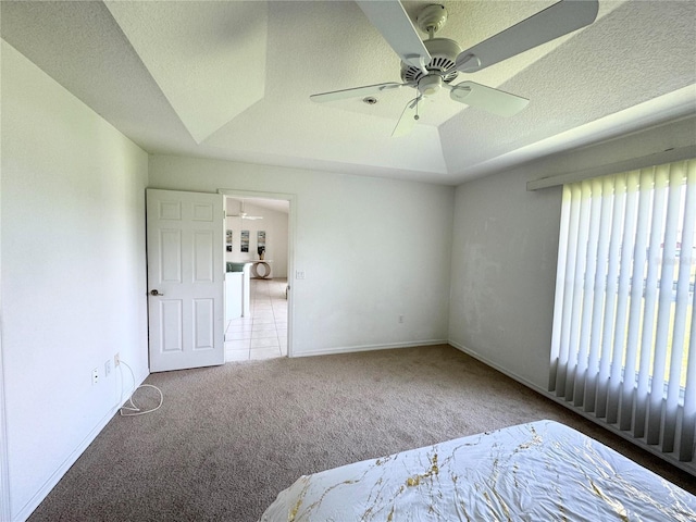 unfurnished bedroom featuring a raised ceiling, light carpet, ceiling fan, a textured ceiling, and baseboards