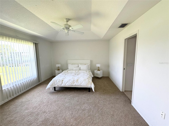 bedroom with a textured ceiling, carpet flooring, ceiling fan, and a raised ceiling