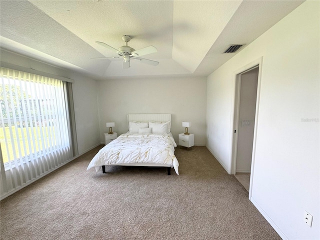 carpeted bedroom with baseboards, visible vents, ceiling fan, a tray ceiling, and a textured ceiling