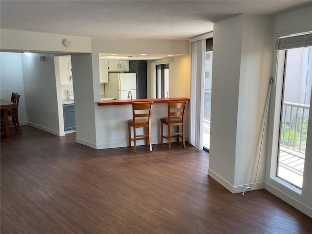 kitchen with a textured ceiling, white cabinets, kitchen peninsula, dark wood-type flooring, and white fridge