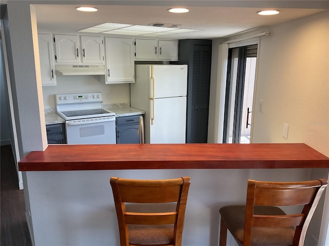 kitchen with a kitchen bar, dark hardwood / wood-style floors, white cabinets, kitchen peninsula, and white appliances