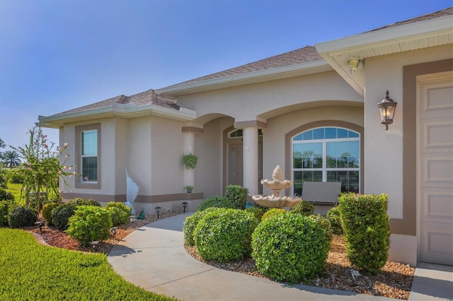 property entrance with a garage, a shingled roof, and stucco siding