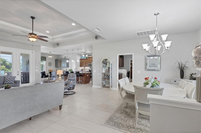 living room with a raised ceiling, ceiling fan with notable chandelier, washer / dryer, french doors, and light tile patterned floors