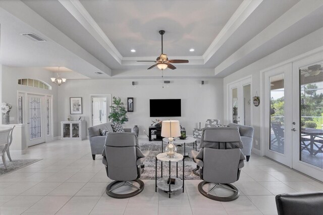 tiled living room featuring ceiling fan with notable chandelier, french doors, and a tray ceiling