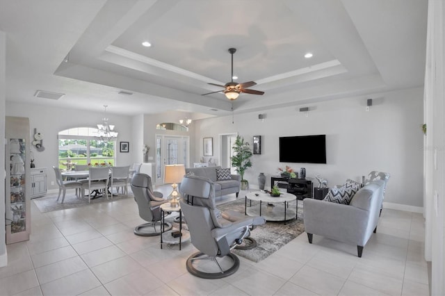 living area featuring visible vents, baseboards, a tray ceiling, light tile patterned flooring, and ceiling fan with notable chandelier