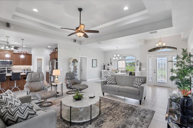 tiled living room with ceiling fan with notable chandelier and a tray ceiling