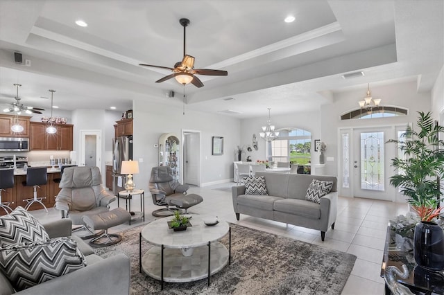 living area with visible vents, ceiling fan with notable chandelier, a tray ceiling, and light tile patterned flooring