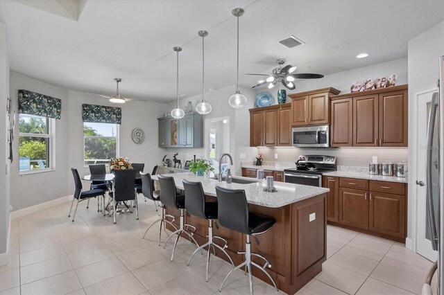 kitchen with ceiling fan, light tile patterned floors, sink, a center island with sink, and stainless steel appliances