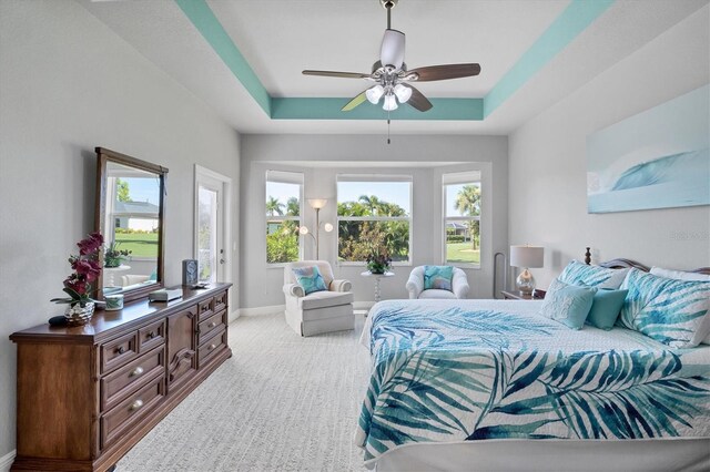 bedroom featuring a tray ceiling, ceiling fan, multiple windows, and light carpet