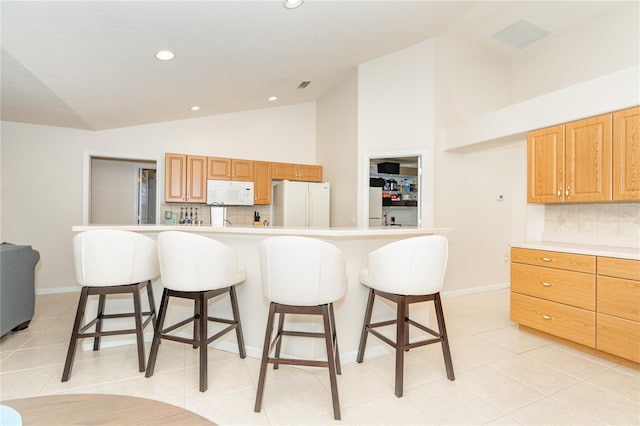 kitchen with white appliances, light tile patterned floors, a kitchen island, a breakfast bar, and light countertops