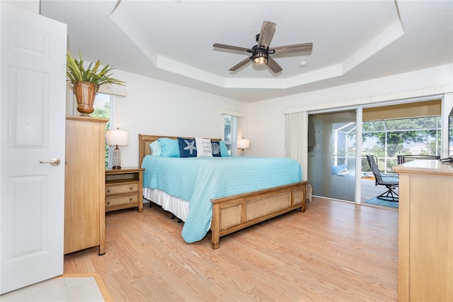 bedroom featuring a ceiling fan, a sunroom, wood finished floors, access to exterior, and a tray ceiling