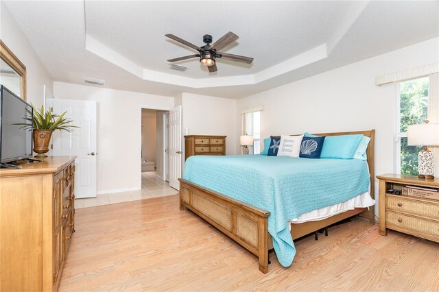 bedroom with ceiling fan, a raised ceiling, connected bathroom, and light hardwood / wood-style flooring