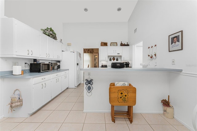 kitchen featuring light tile patterned floors, a high ceiling, white refrigerator with ice dispenser, white cabinetry, and kitchen peninsula