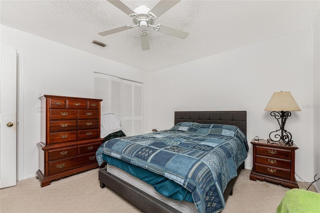 bedroom featuring visible vents, light colored carpet, ceiling fan, a textured ceiling, and a closet