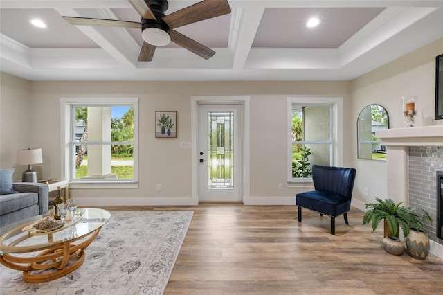 living room with ceiling fan, coffered ceiling, light wood-type flooring, a fireplace, and ornamental molding