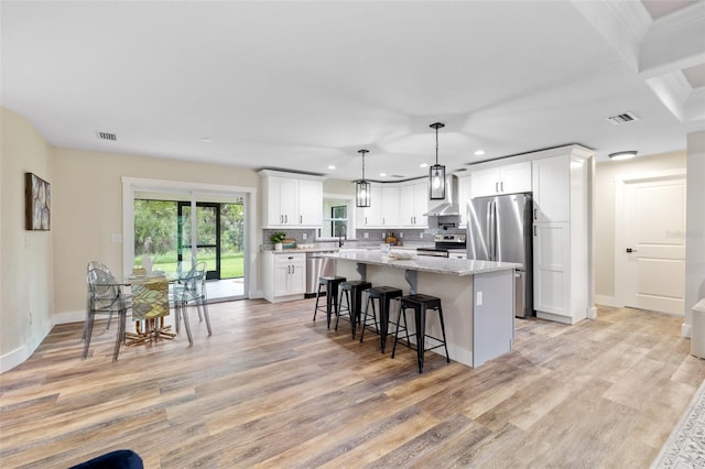 kitchen featuring light wood-type flooring, stainless steel appliances, decorative light fixtures, white cabinets, and a kitchen island