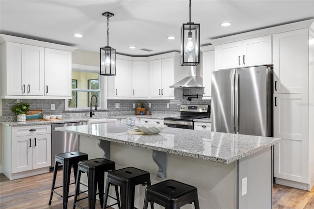 kitchen featuring white cabinets, light stone countertops, light wood-type flooring, a kitchen island, and stainless steel appliances