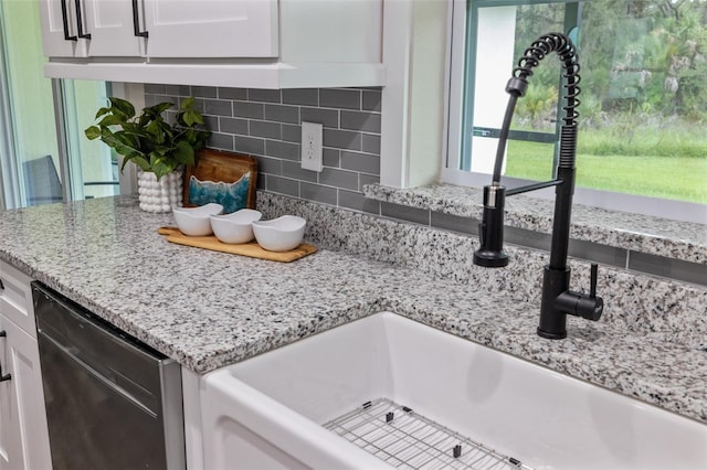 details featuring sink, tasteful backsplash, light stone counters, stainless steel dishwasher, and white cabinets