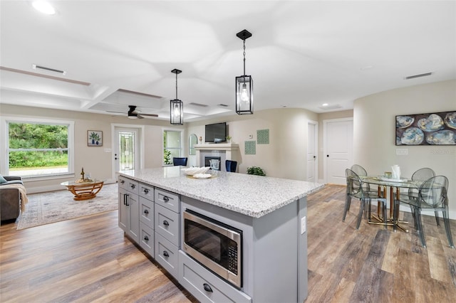 kitchen with hanging light fixtures, a center island, stainless steel microwave, and dark wood-type flooring