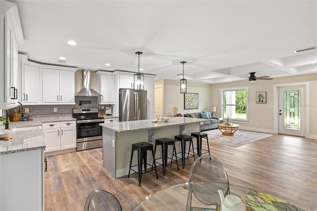 kitchen featuring wall chimney exhaust hood, stainless steel appliances, white cabinetry, light hardwood / wood-style flooring, and a kitchen island