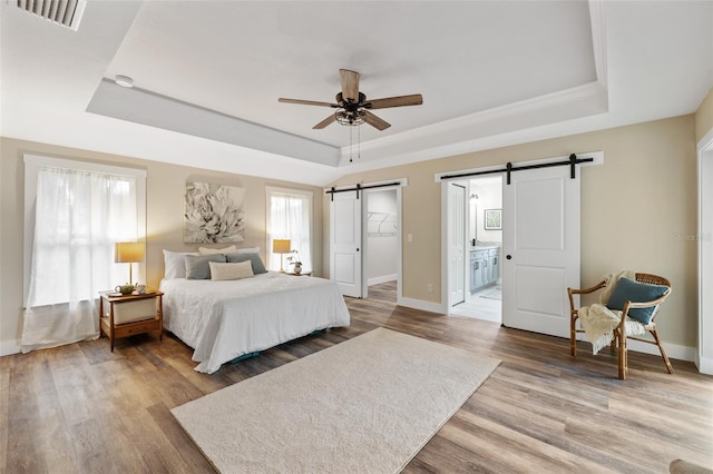 bedroom featuring a tray ceiling, ensuite bath, ceiling fan, and hardwood / wood-style flooring