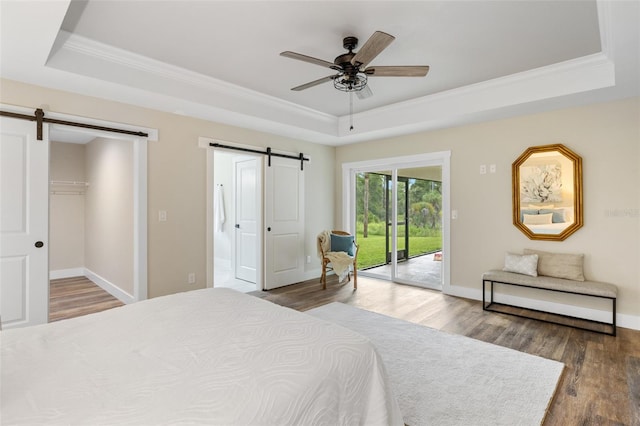 bedroom with hardwood / wood-style floors, access to outside, ceiling fan, a barn door, and a tray ceiling