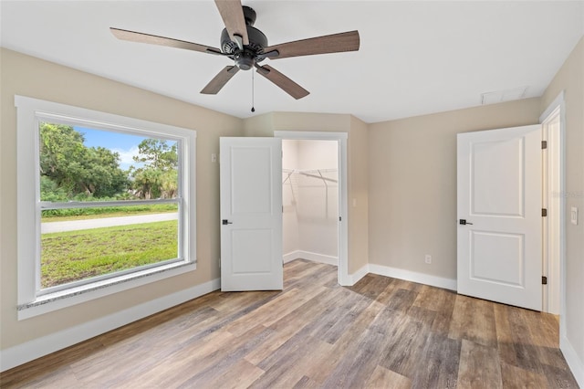 unfurnished bedroom featuring a closet, a spacious closet, light hardwood / wood-style flooring, and ceiling fan