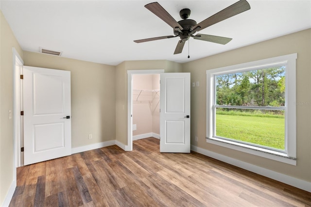 unfurnished bedroom featuring ceiling fan, light wood-type flooring, a spacious closet, and a closet