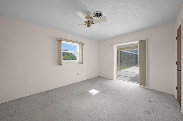 spare room featuring light colored carpet, ceiling fan, visible vents, and a textured ceiling