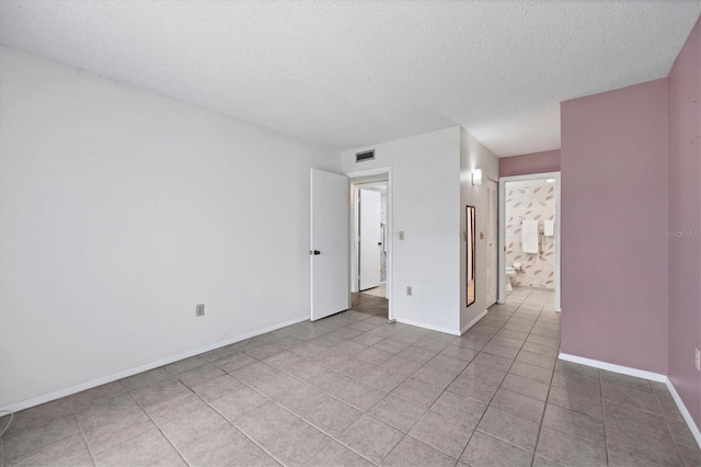 unfurnished bedroom with connected bathroom, a textured ceiling, and light tile patterned floors