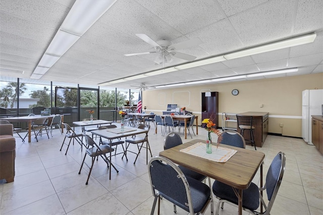 tiled dining space with a paneled ceiling, floor to ceiling windows, and ceiling fan