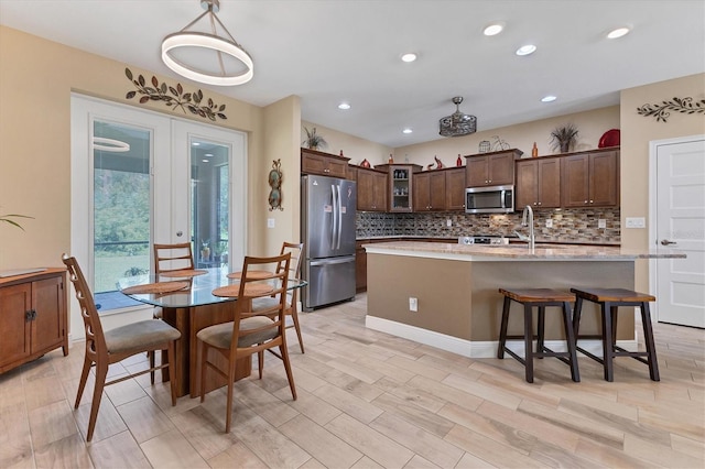 kitchen with appliances with stainless steel finishes, dark brown cabinets, a center island with sink, backsplash, and sink