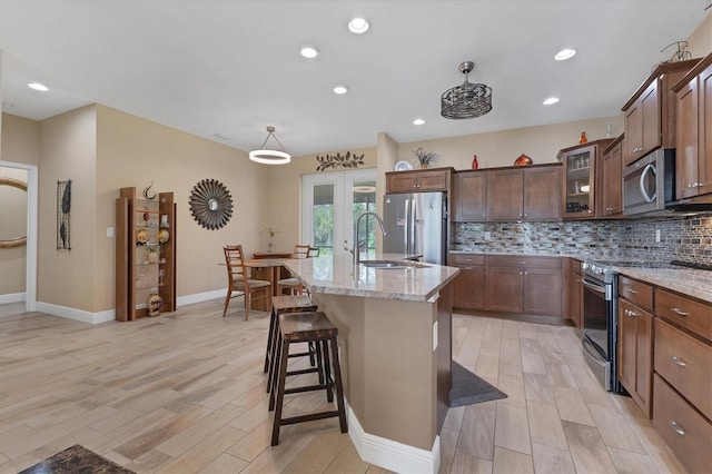 kitchen featuring stainless steel appliances, decorative backsplash, light stone countertops, an island with sink, and sink