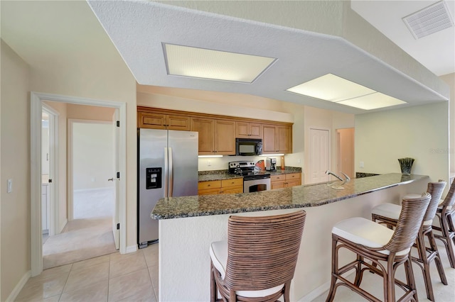 kitchen featuring dark stone countertops, a kitchen breakfast bar, appliances with stainless steel finishes, and light tile patterned floors