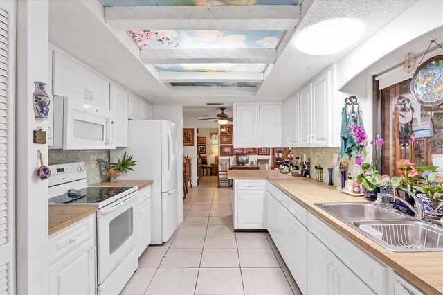 kitchen featuring ceiling fan, decorative backsplash, a tray ceiling, sink, and white appliances