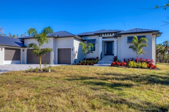 prairie-style house featuring metal roof, a front lawn, an attached garage, and stucco siding