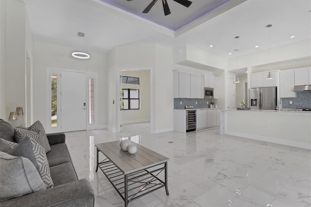 living room with ceiling fan, a towering ceiling, beverage cooler, and a tray ceiling