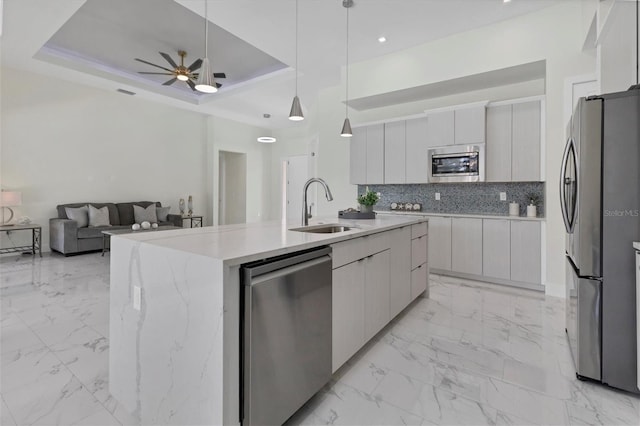 kitchen with stainless steel appliances, a sink, marble finish floor, a tray ceiling, and modern cabinets