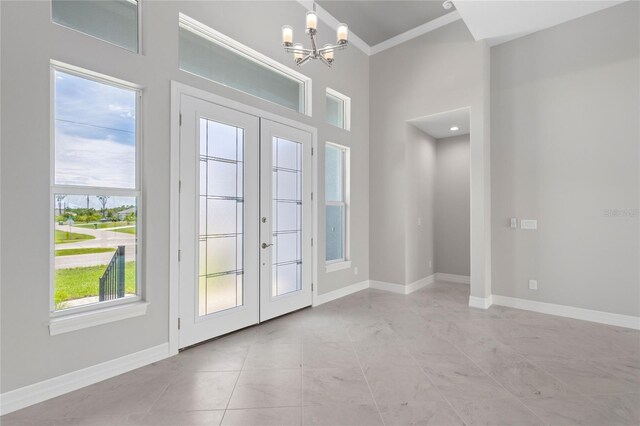 entryway with tile patterned flooring, a notable chandelier, crown molding, and french doors